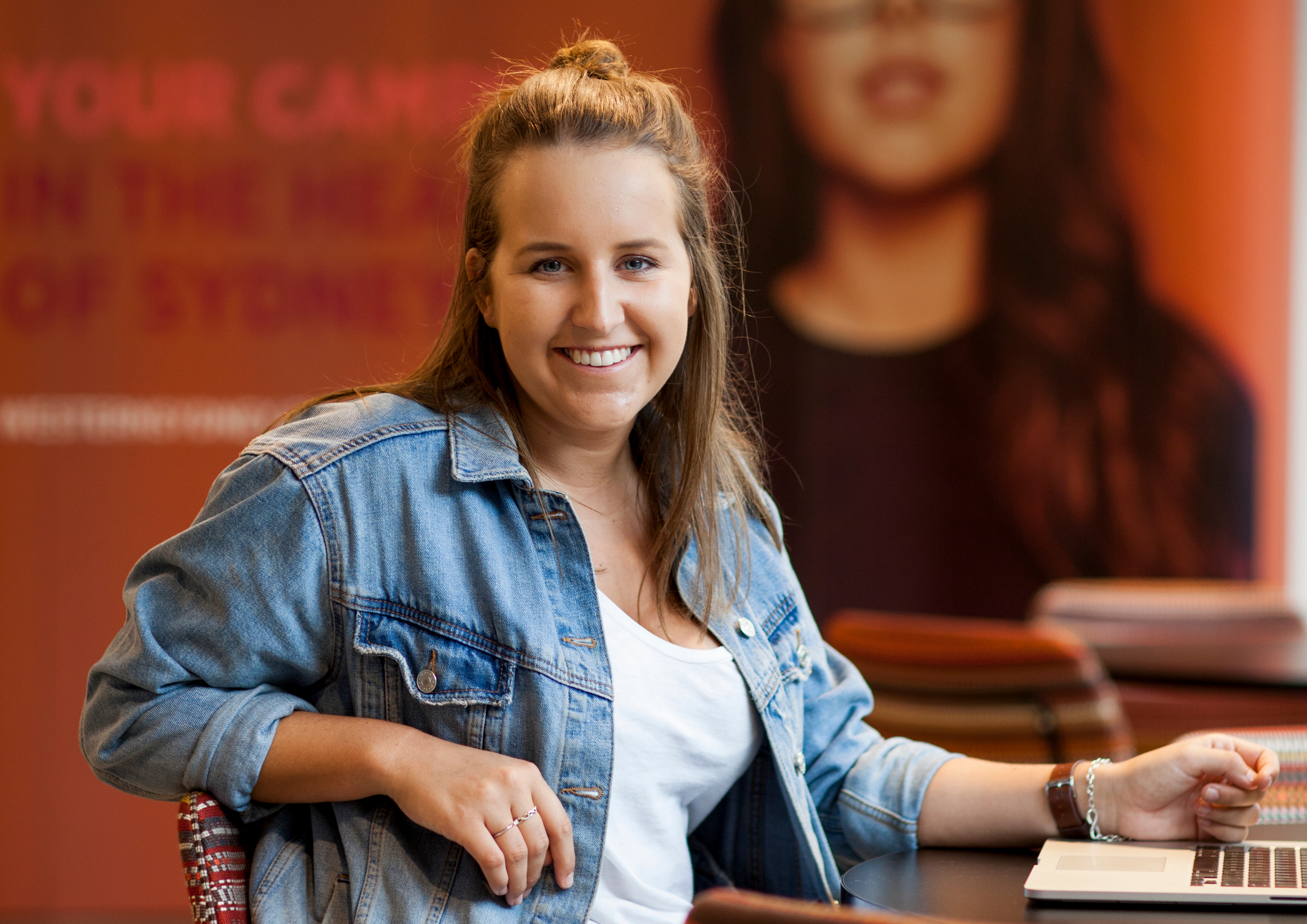 Female student wearing denim jacket and sitting at a desk with a laptop.